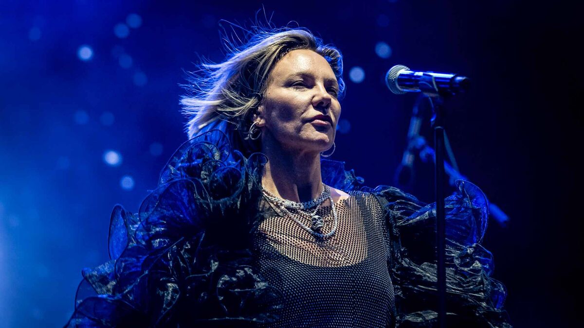 Kate Ryan występuje na scenie przy mikrofonie, ubrana w czarną kreację z obszernymi, dekoracyjnymi rękawami. Ma krótkie blond włosy, duże kolczyki i kilka srebrnych naszyjników. W tle widoczne jest niebieskie oświetlenie sceniczne i rozproszone punkty światła.
